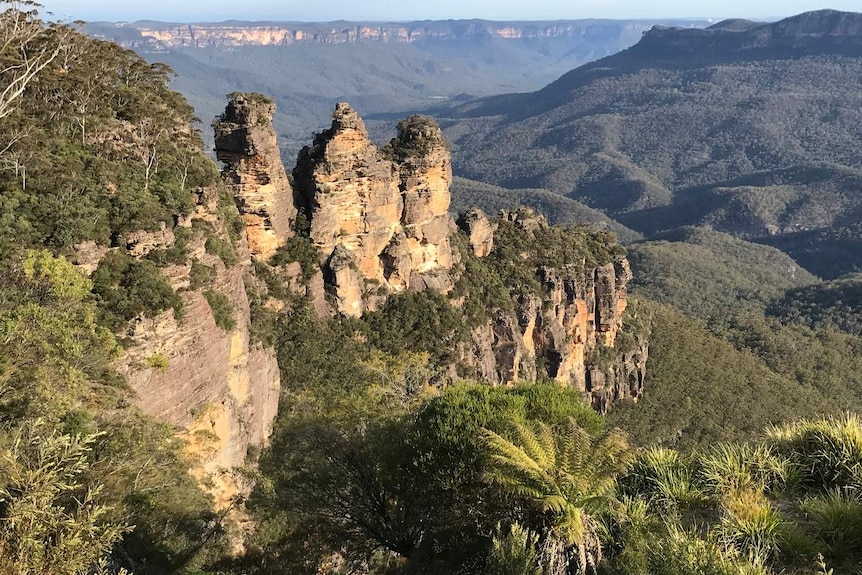 a three-pronged rock formation in green mountain ranges