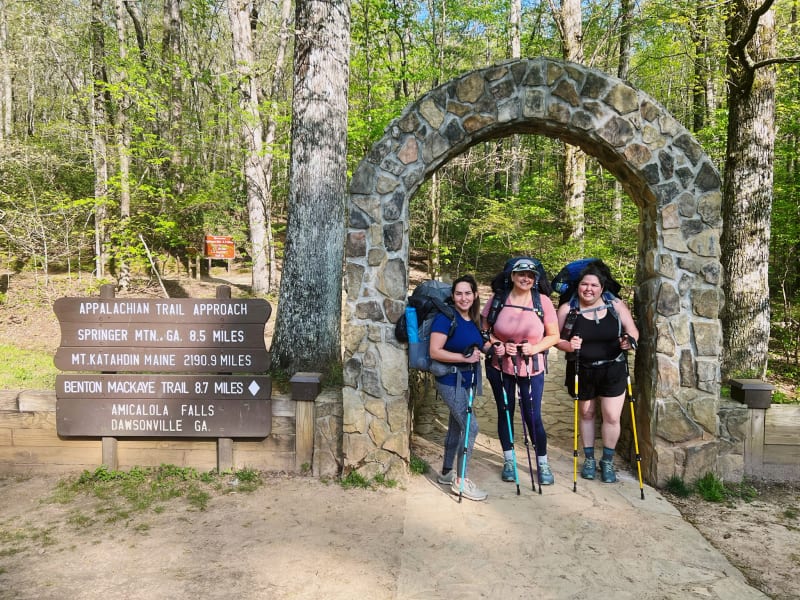 Three smiling women under the arch at the start of the Appalachian Trail Approach.