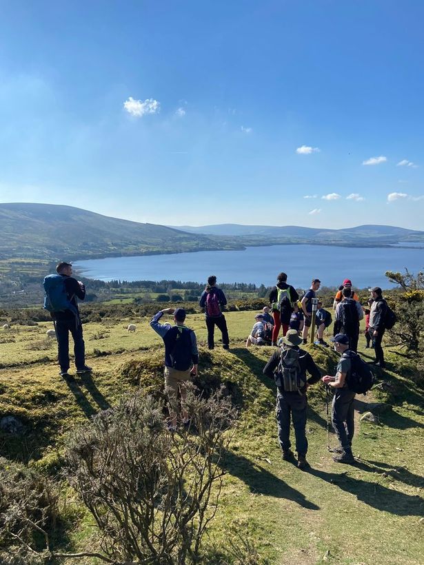 Out & About Hiking members explore beautiful nature above a lake on a mountain in Ireland under blue skies