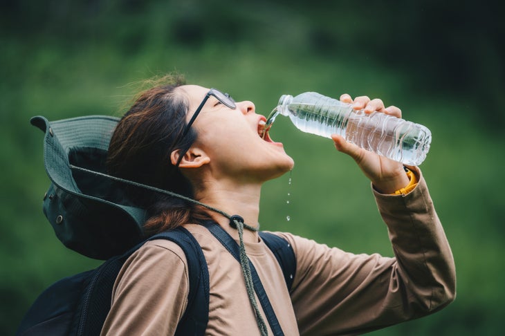 Asian woman drinking water from plastic bottle while hiking